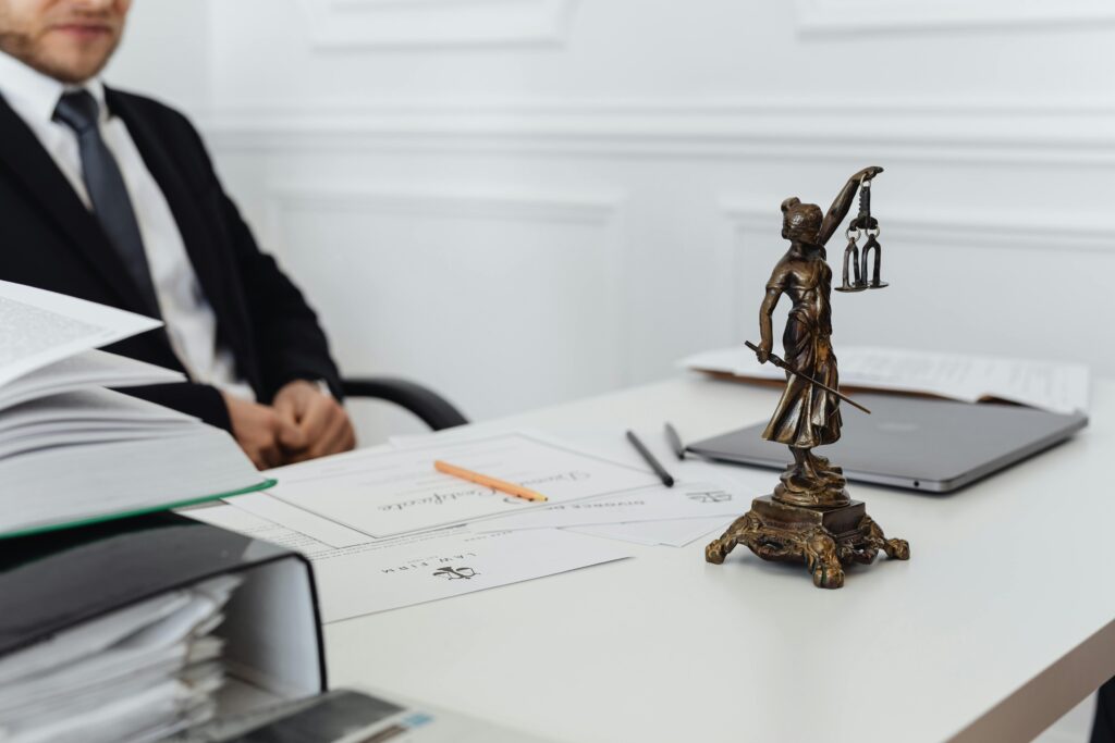 pexels-photo-7876093-7876093 A legal professional's workspace featuring Lady Justice statue, documents, and a laptop.